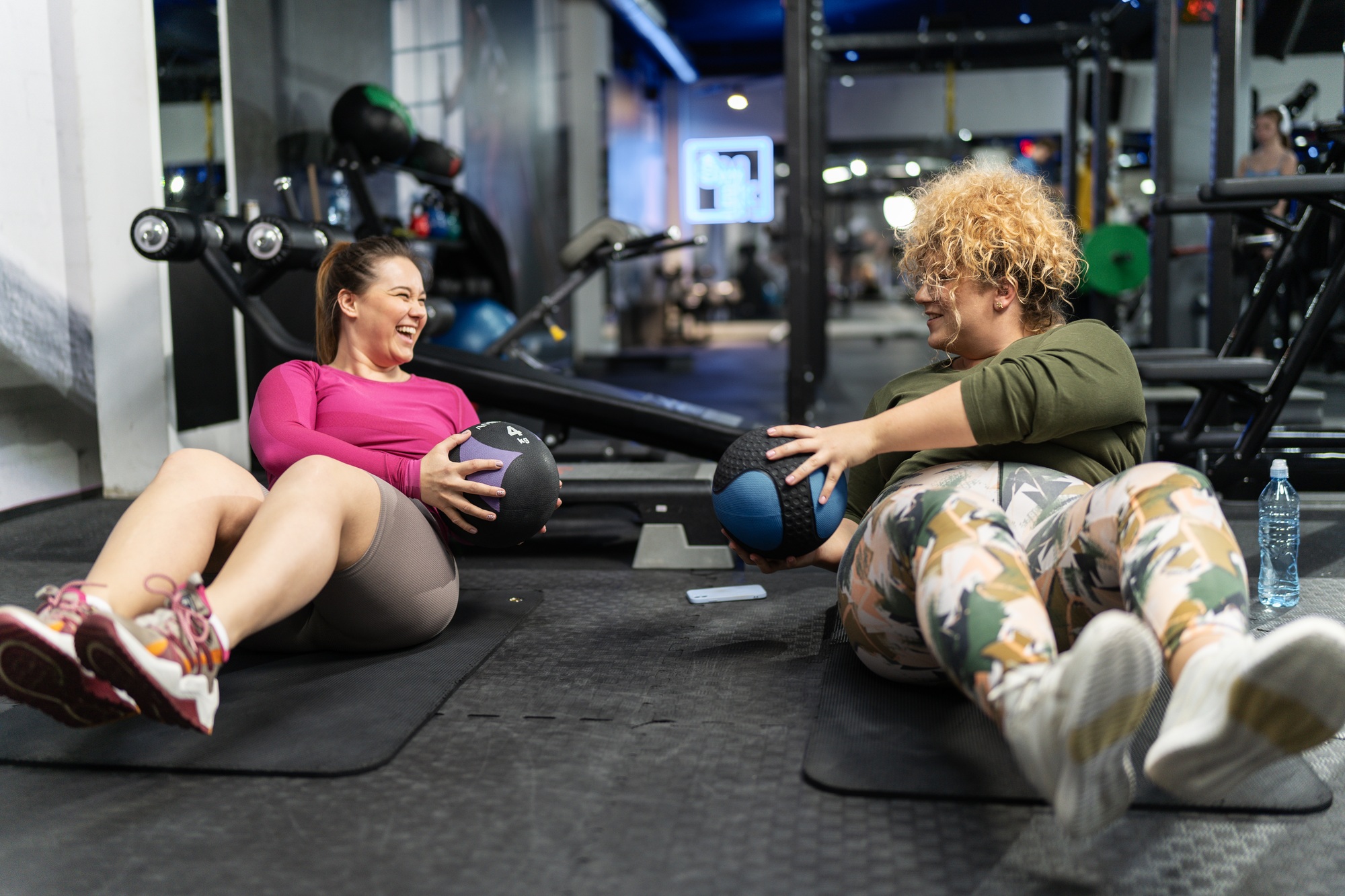 Two plus-size women embrace their bodies as they engage in a challenging workout.